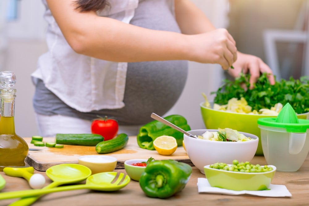 glückliche schwangere frau kocht gemüse