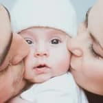 Frischgebackene Eltern küssen ihr Neugeborenes liebevoll und zeigen enge Familienbindung
