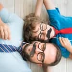Vater und Kind mit lustigen Fake-Schnurrbärten und Brillen zeigen spielerischen Väterinstinkt und liebevolle Vater-Kind-Bindung