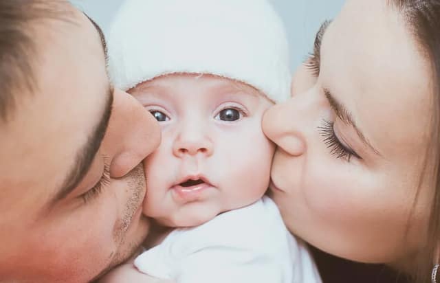 Frischgebackene Eltern küssen ihr Neugeborenes liebevoll und zeigen enge Familienbindung