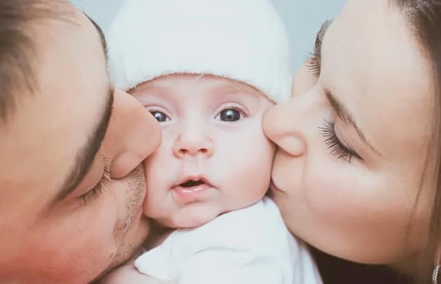 Frischgebackene Eltern küssen ihr Neugeborenes liebevoll und zeigen enge Familienbindung