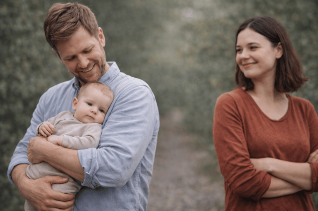 Vater hält Baby im Arm während Mutter daneben steht als Beispiel für Kind erziehen ohne Beziehung in Co-Elternschaft