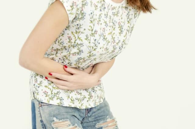 PID Symptome Frau mit starken Unterleibsschmerzen hält ihren Bauch und wirkt erschöpft