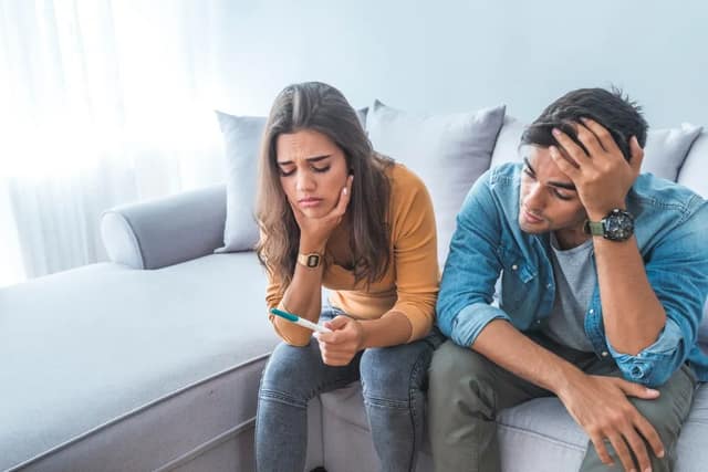 Stress Schwangerschaft Paar sitzt besorgt mit negativem Schwangerschaftstest auf dem Sofa