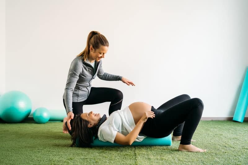 Schwangere Frau macht Pilates-Übungen und Fitnessball mit Trainer