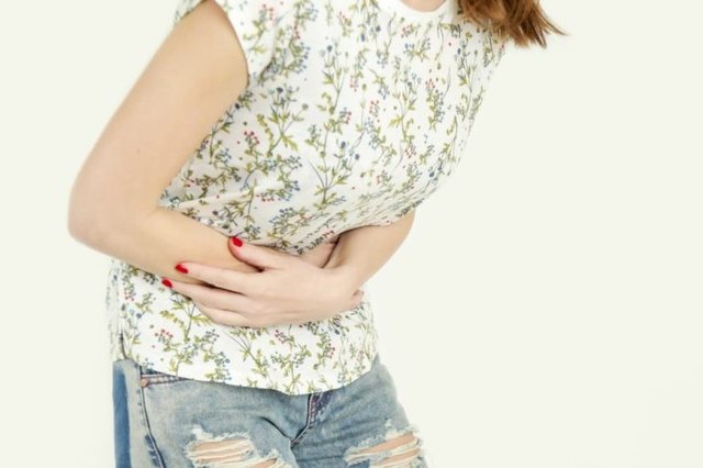 PID Symptome Frau mit starken Unterleibsschmerzen hält ihren Bauch und wirkt erschöpft