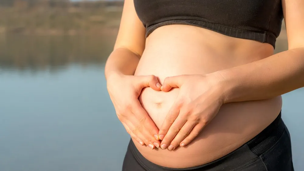 Leihmutter im Ausland schwangere Frau hält ihren Bauch mit beiden Händen im Freien