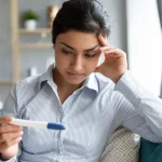 Schwangerschaft Wartezeit Frau schaut besorgt auf einen Schwangerschaftstest und wartet auf das Ergebnis