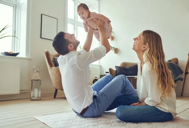 Tipps Co-Elternschaft glückliches Elternpaar spielt gemeinsam mit ihrem Baby im Wohnzimmer