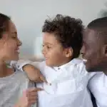 Lächelnde junge multiethnische Eltern, die sich umarmen, zum Thema Fragen Co-Elternteil