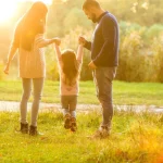Familie mit Kind spaziert glücklich im Park bei Sonnenuntergang, symbolisiert das Wechselmodell bei getrennt lebenden Eltern