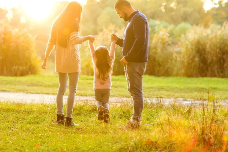 Familie mit Kind spaziert glücklich im Park bei Sonnenuntergang, symbolisiert das Wechselmodell bei getrennt lebenden Eltern